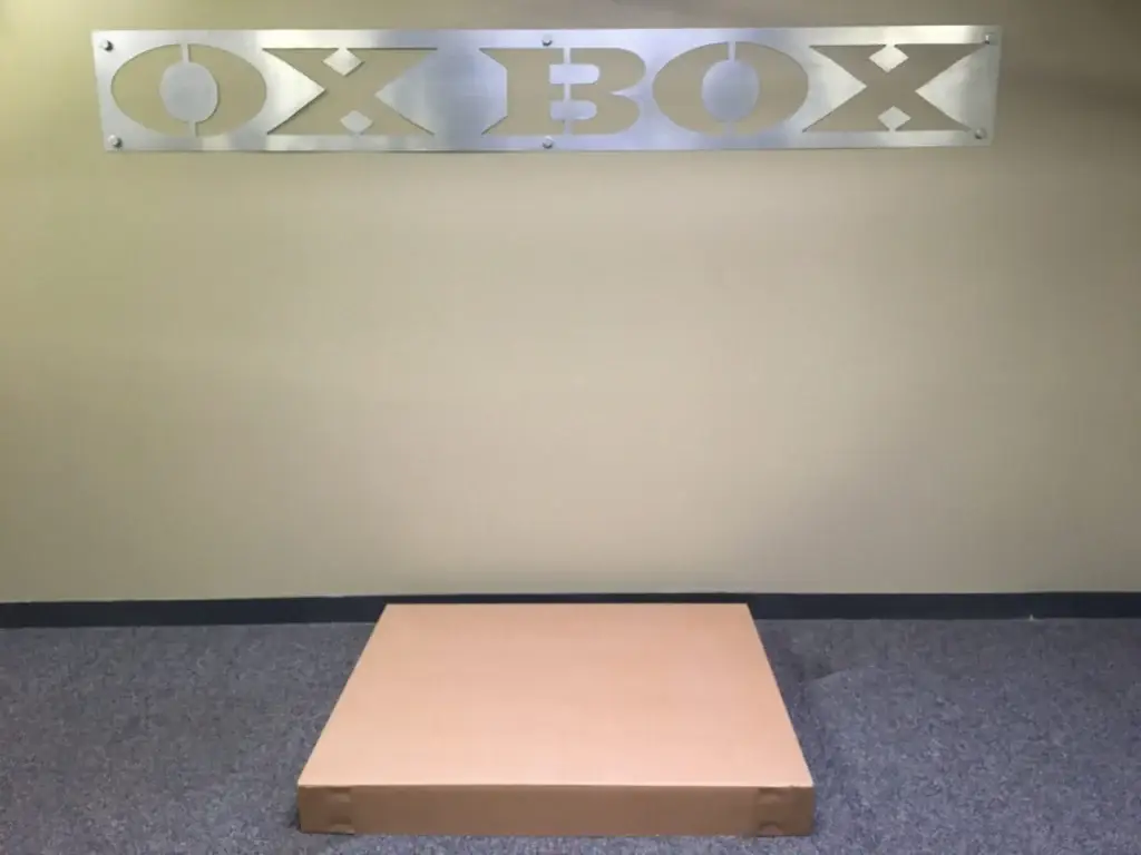 Brown cardboard box on carpeted floor beneath a metallic sign reading "OX BOX.